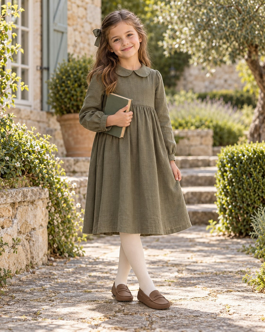 Girl in a long-sleeved sage dress and opaque tights wearing London Kids brown moccasins.